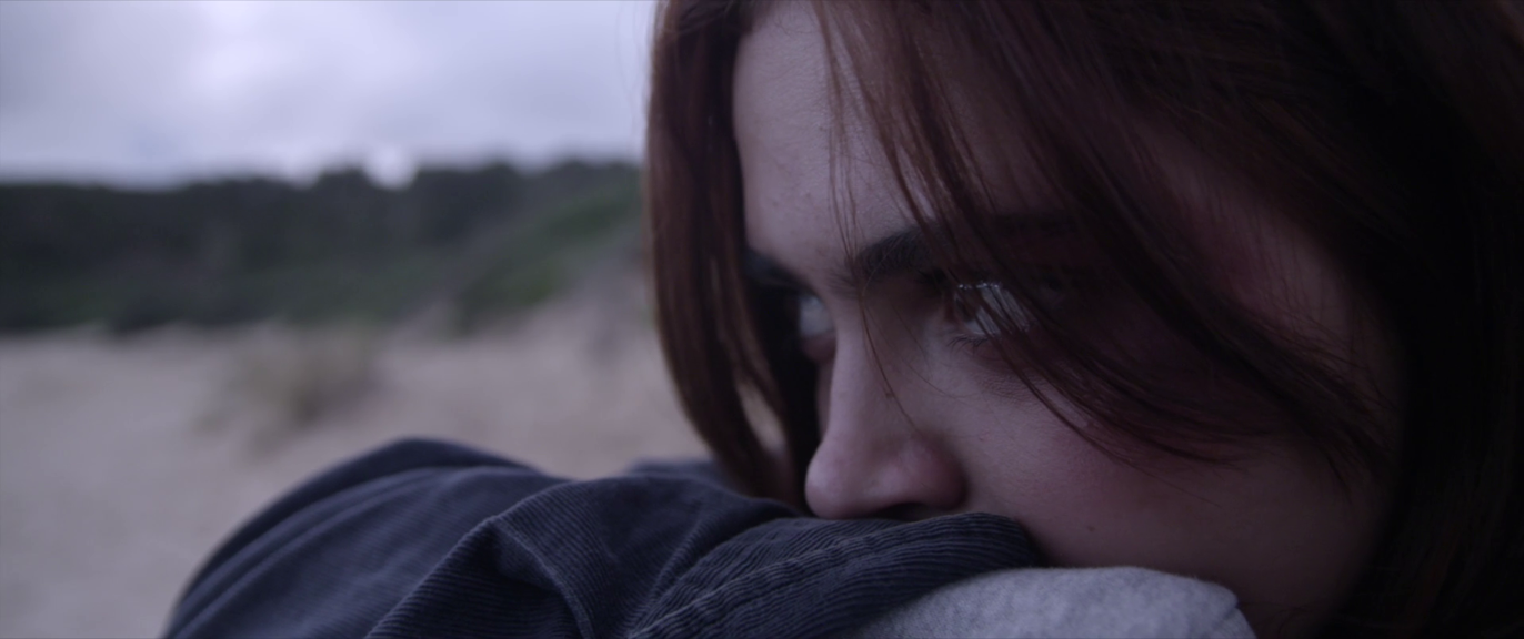 A close up of a young girl at the beach covering her mouth with her forearm.