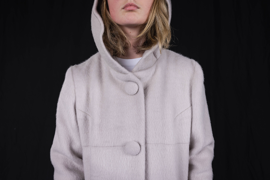 A close up image of a person wearing a buttoned up faux fur coat with a hood.