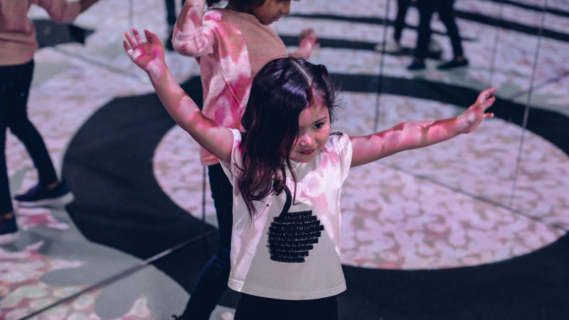 Children dancing in front of mirrors with projections on their arms and bodies