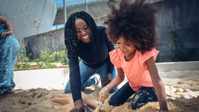 Mother and daughter in sand with a paintbrush, uncovering a fossil