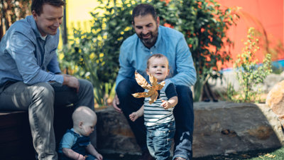 Two men and a baby, and a toddler with a leaf, sitting in the garden