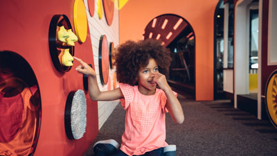 Girl pointing at her nose and at a yellow nose on the wall