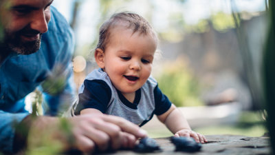 Man and baby touching brass frogs on a rock outside