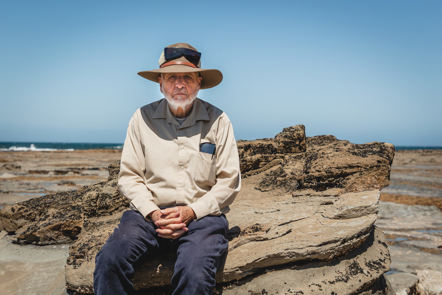 a man wearing a hat sits in the sun on the beach