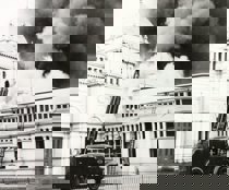 Four men in shorts holding picks sitting on recently dug ground in front of the Exhibition Building. 