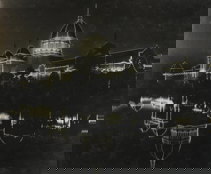 Exhibition Building decorated with lights at night, lake in foreground.