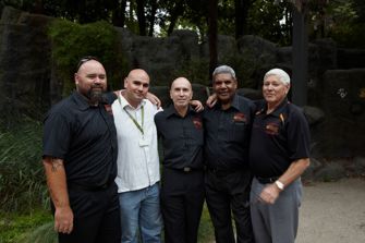 A group of five men with their arms around each others shoulders.