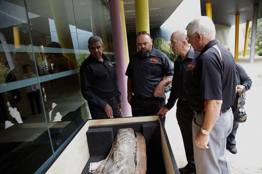 Group of four men looking into a box with a carving in it.