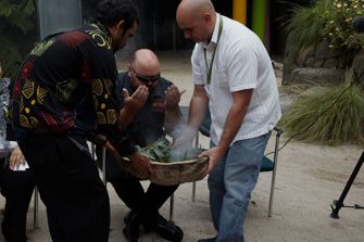 Two men holding a bowl while another man wafts the smoke towards himself