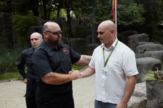 Two men shaking hands. A third man looks on.