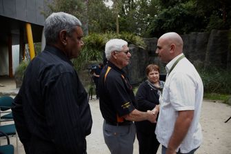 Two men shake hands. A man and a woman look on.