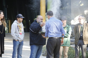 People looking on at a man holding a small bowl of smoke