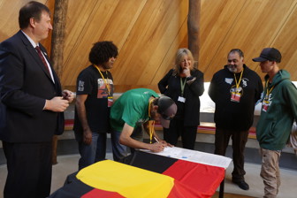 Man signing documents. Five people looking on.