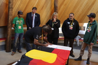 Man signing documents. Five people look on.