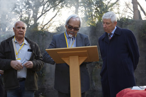 A man signing documents. Two other men look on.