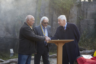 Two men shaking hands. On man looking on.