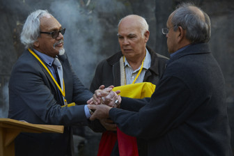 Three men standing in a group. Two clasping hands. On holding a box wrapped in the Aboriginal flag.