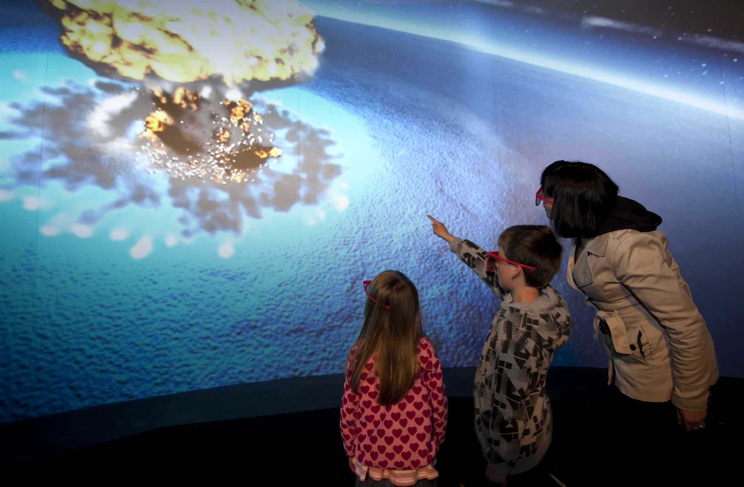 A woman and 2 children pointing at a large screen