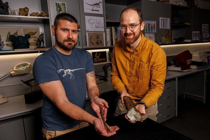 Two men looking towards the camera each holding a fossils