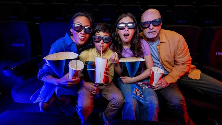 Family of four eating popcorn and drinking soft drink at IMAX.