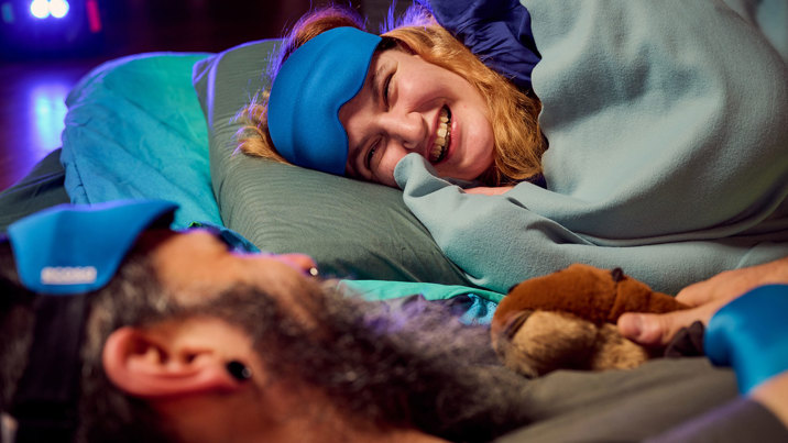 A woman smiling while sleeping under the dinosaurs during Adult Museum Sleepovers at Melbourne Museum.