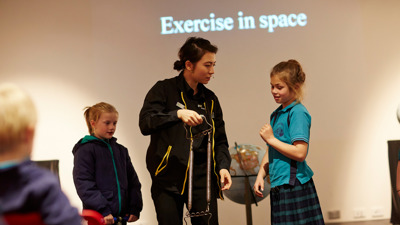 A Scienceworks presenter guides two student volunteers through a demonstration about exercising in space during the Blast Off show.