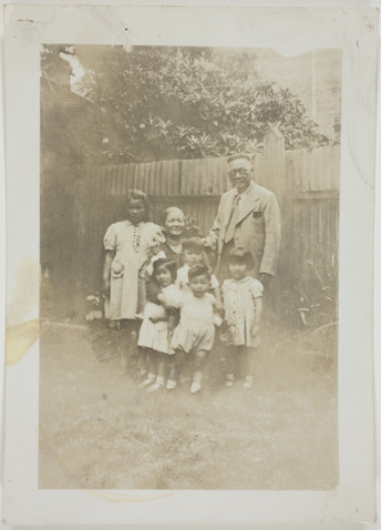 Photo of Sydney and May Gung, and five of their grandchildren taken in a back yard in front of fence.