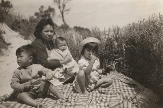 Woman with three young children sitting on a blacket on a beach.