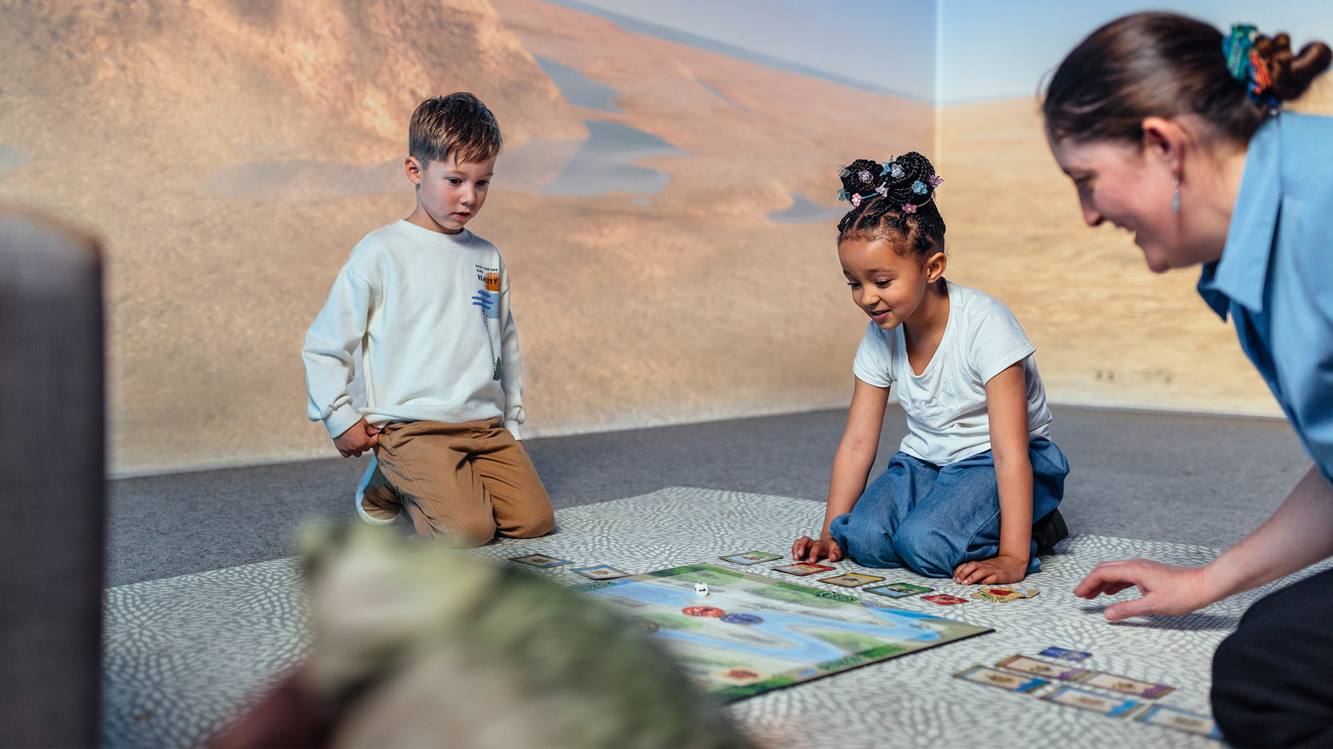 A teacher and two young children playing a board game.
