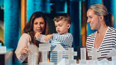A child standing between two people playing with white block in an exhibition