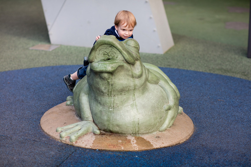 Child climbing on Tiddalik, the frog statue, in the water play area in the Children's Gallery outdoor playground