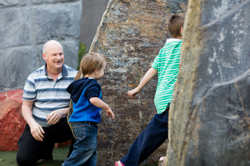 Man watching two children run through a rock garden