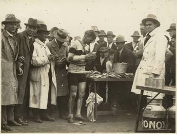 Cyclist eating a sandwich in crowd of onlookers.