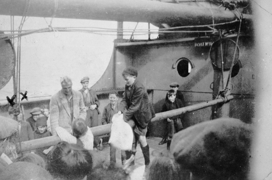 Small boys on a greasy pole on the SS Beltana. One boy is straddling the pole while another is leaning against it. There are two crosses marking the boy on the far left.