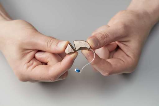 Two hands holding a hearing aid