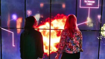 Two women in front of large video screen displays