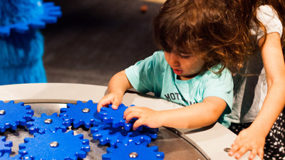 Child playing with blue cogs in the Ground Up exhibition 
