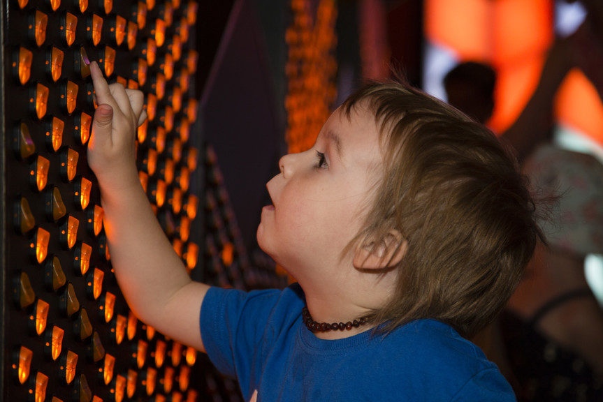 Boy touching the button switches on wall interactive in Ground Up exhibition at Scienceworks. 