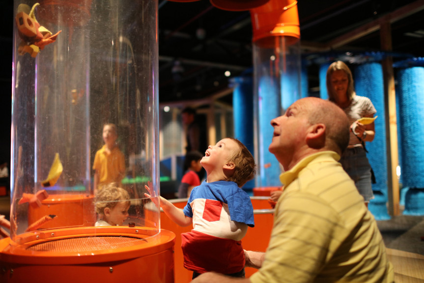 Family playing with suction tubes in the Ground Up exhibition at Scienceworks. 