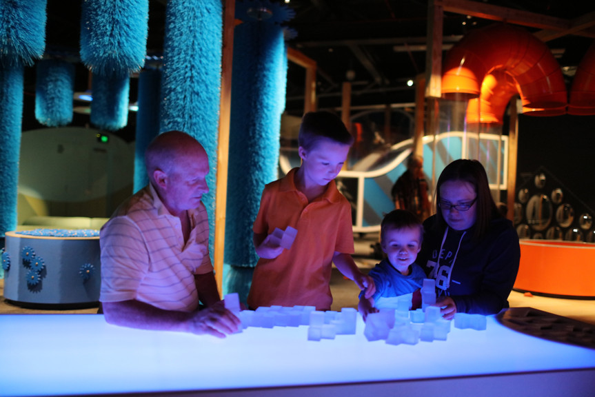 Family playing with building blocks on the light-up table in the Ground Up exhibition at Scienceworks. 