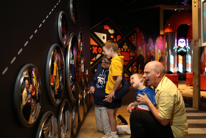 Family playing with the mirror wall in the Ground Up exhibition at Scienceworks. 