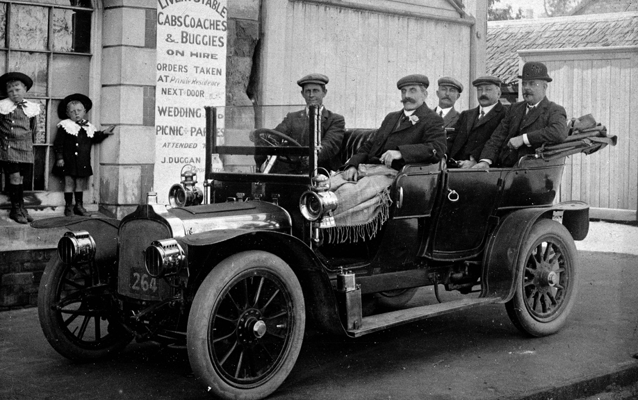 An early motor car with wooden-spoked wheels and an open touring body parked in front of J. Dyggan's Livery Stables in Castlemaine. 