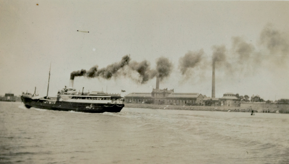 View of Spotswood Pumping Station eastern frontage taken from eastern river bank, circa 1930s. Shows both chimneys, North Straining House, residence and part of Australian glass works wall. Note SS Edina sailing down the river in front of the Pumping Station.