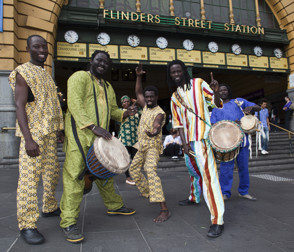 Group of men under the clocks at Flinders Street. Three are holding drums