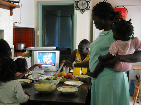 Family around a dinner table eating and watch television