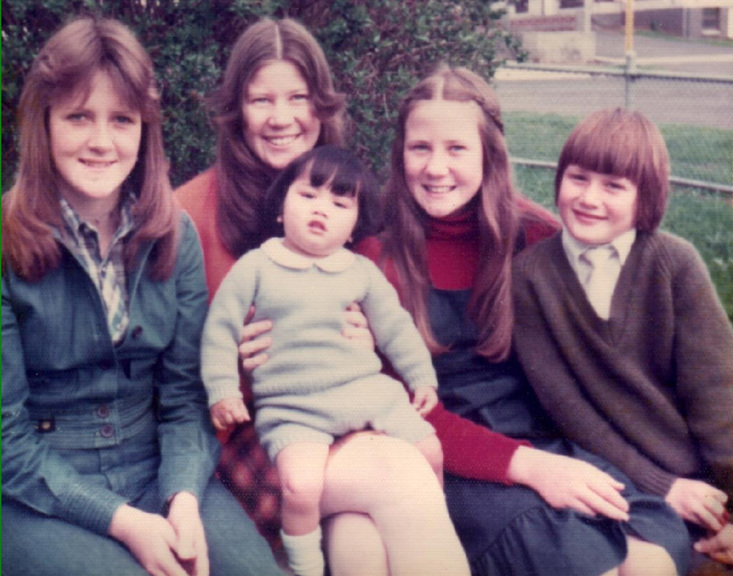 Photograph of a group of children. Girl second from the left is holding a baby