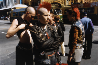 Group of people stand in the street. The person in the centre of the photograph has a red mohawk