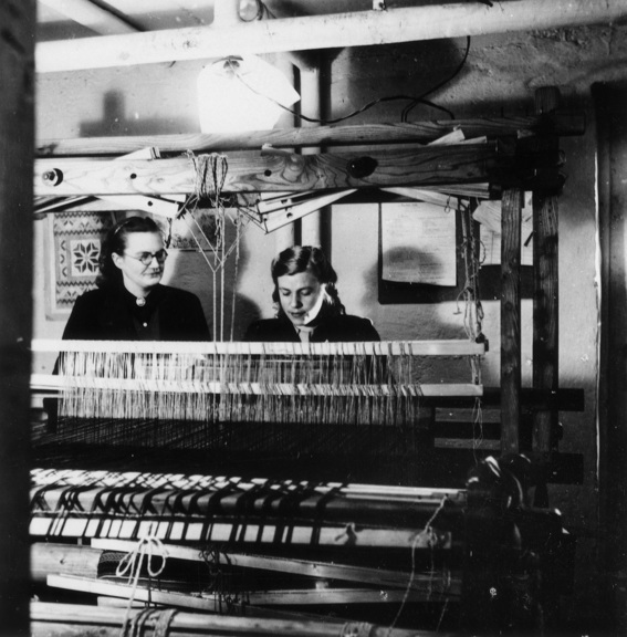 Black and white photograph of two women sitting at a weaving loom