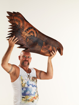 Artist Mick Harding holding aloft his wooden carving of Bunjil