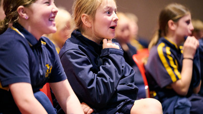 A young girl watching a science show looks amazed at what she’s seeing